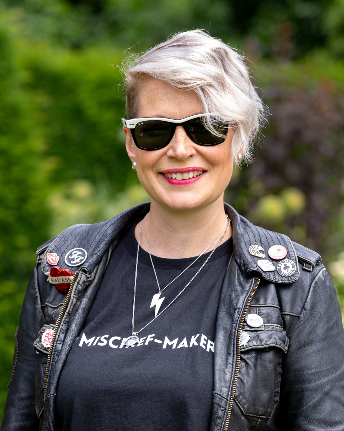 Zoe in sunglasses and a Mischief-Maker tee, smiling in a garden